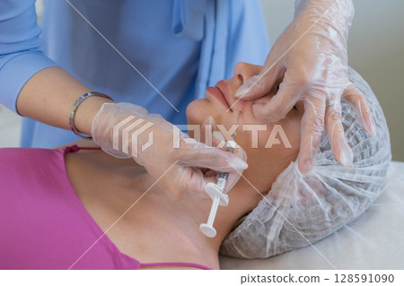 Medical professional administers a precise injection, a common aesthetic procedure. This represents the attention to detail in modern cosmetology. Medical professional administers a precise injection, a common aesthetic procedure. This represents the attention to detail in modern cosmetology. 128591090