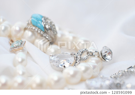 Close-up of elegant jewelry pieces, including pearls, silver rings, and a blue gemstone ring on a white fabric background. This image captures the luxury and sophistication of fine jewelry 128591099