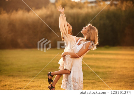 Holding girl in hands. Woman with her daughter is on the summer field Holding girl in hands. Woman with her daughter is on the summer field 128591274