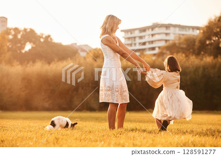 Dancing, having fun. Mother with her daughter and cute dog are on the field outdoors Dancing, having fun. Mother with her daughter and cute dog are on the field outdoors 128591277