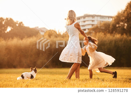 Dancing, having fun. Mother with her daughter and cute dog are on the field outdoors 128591278