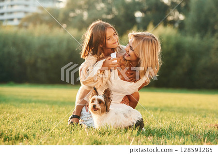 Positive emotions, on the green grass. Mother with her daughter and cute dog are on the field outdoors Positive emotions, on the green grass. Mother with her daughter and cute dog are on the field outdoors 128591285