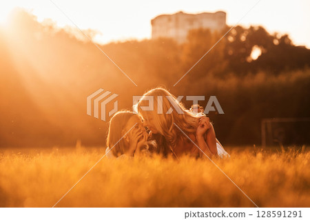 Illuminated by sunlight, lying down. Mother with her daughter and cute dog are on the field outdoors Illuminated by sunlight, lying down. Mother with her daughter and cute dog are on the field outdoors 128591291