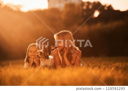 Illuminated by sunlight, lying down. Mother with her daughter and cute dog are on the field outdoors 128591293