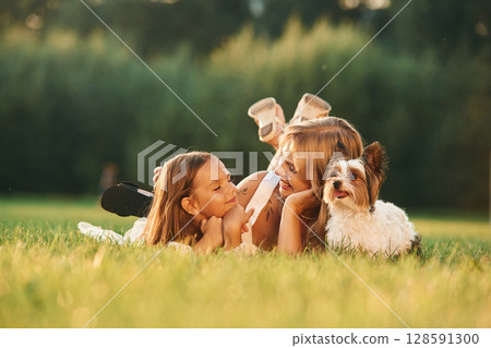 Positive emotions, on the green grass. Mother with her daughter and cute dog are on the field outdoors Positive emotions, on the green grass. Mother with her daughter and cute dog are on the field outdoors 128591300