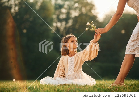 Taking little flowers from parent. Woman with her daughter is on the summer field Taking little flowers from parent. Woman with her daughter is on the summer field 128591301