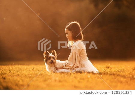 Illuminated by sunlight. Cute little girl is on the field with dog 128591324