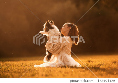 Illuminated by sunlight. Cute little girl is on the field with dog 128591326