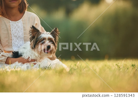 Dog in hands of cute little girl that is on the field 128591343