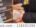 Close-Up of Hands Holding a White Wallet in a Shopping Environment 128591394