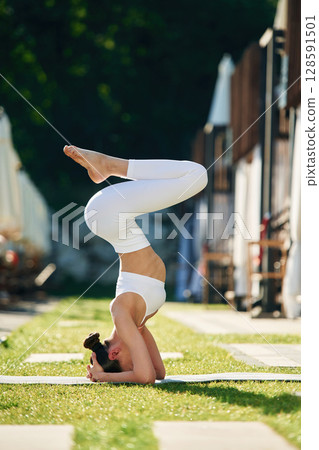 Doing head stand. Young woman in yoga clothes is outdoors 128591501