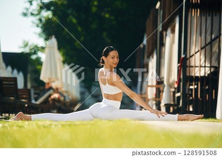 Focused on exercises. Young woman in yoga clothes is outdoors Focused on exercises. Young woman in yoga clothes is outdoors 128591508