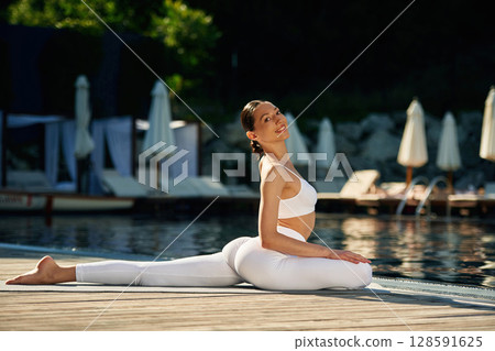 Sitting on twine. Woman near pool is doing yoga exercises 128591625