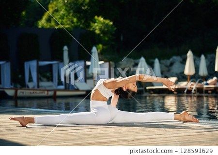 Flexible body. Woman near pool is doing yoga exercises 128591629