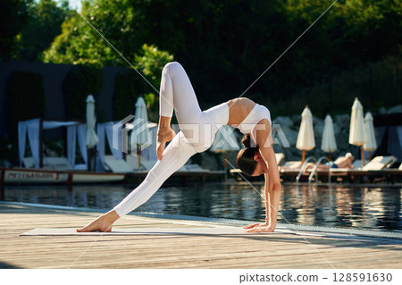 Flexible body. Woman near pool is doing yoga exercises 128591630