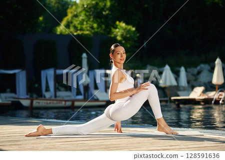 Doing professional exercises. Woman near pool is doing yoga Doing professional exercises. Woman near pool is doing yoga 128591636