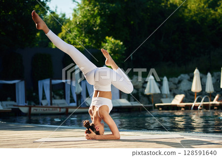 Front view. Woman near pool is doing yoga exercises 128591640