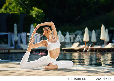 Front view. Woman near pool is doing yoga exercises 128591642