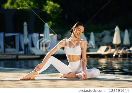 Front view. Woman near pool is doing yoga exercises 128591644