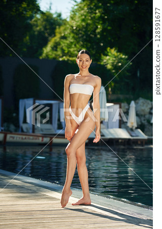 Trees with green leaves at background. Woman in white underwear is near the pool Trees with green leaves at background. Woman in white underwear is near the pool 128591677
