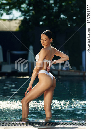 Smiling and standing. Woman in white underwear is in the pool 128591725
