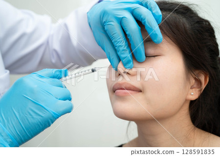 Asian woman receiving plastic surgery shape of nose performed on face. Asian woman receiving plastic surgery shape of nose performed on face. 128591835