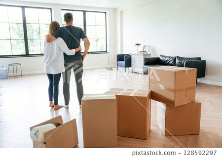 Looking at the big windows. Young couple moving to new home Looking at the big windows. Young couple moving to new home 128592297