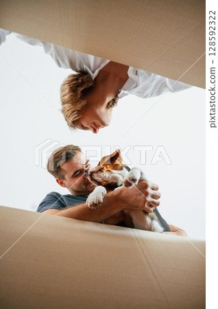 Holding dog and looking into a box. Young couple are moving to new home Holding dog and looking into a box. Young couple are moving to new home 128592322