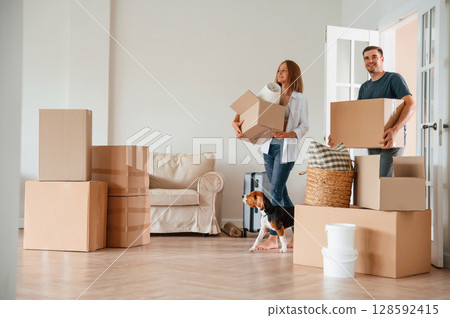 Walking forward with boxes. Young couple with dog are moving to new home Walking forward with boxes. Young couple with dog are moving to new home 128592415