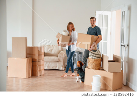 Walking forward with boxes. Young couple with dog are moving to new home 128592416