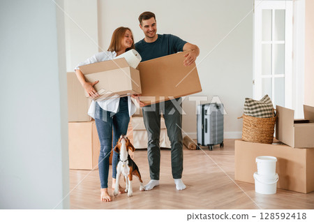 Walking forward with boxes. Young couple with dog are moving to new home 128592418