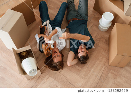 On the floor, lying down, top view. Young couple with dog are moving to new home On the floor, lying down, top view. Young couple with dog are moving to new home 128592459