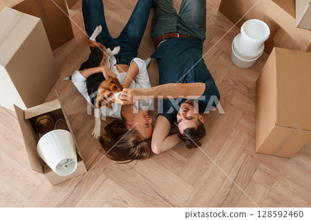 On the floor, lying down, top view. Young couple with dog are moving to new home On the floor, lying down, top view. Young couple with dog are moving to new home 128592460