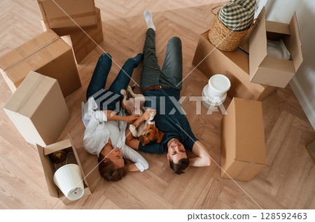 On the floor, lying down, top view. Young couple with dog are moving to new home On the floor, lying down, top view. Young couple with dog are moving to new home 128592463