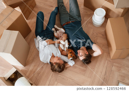 Between boxes, lying down. Young couple with dog are moving to new home Between boxes, lying down. Young couple with dog are moving to new home 128592466