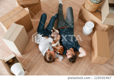 Between boxes, lying down. Young couple with dog are moving to new home 128592467