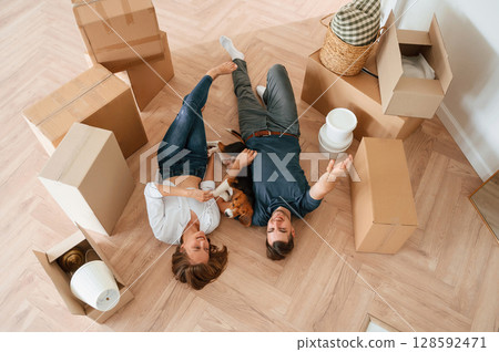 Happy young couple with dog are moving to new home. Lying down on the floor Happy young couple with dog are moving to new home. Lying down on the floor 128592471