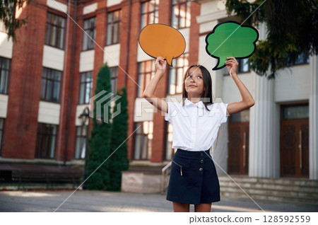 Colorful stickers in hands, copy space for text, thoughts. School girl in uniform is outdoors near the building Colorful stickers in hands, copy space for text, thoughts. School girl in uniform is outdoors near the building 128592559