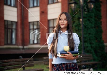 An apple on the books. School girl in uniform is outdoors near the building 128592573