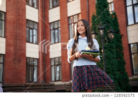 An apple on the books. School girl in uniform is outdoors near the building 128592575