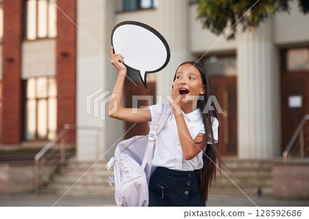 Holding sign with copy space for text. School girl in uniform is outdoors near the building Holding sign with copy space for text. School girl in uniform is outdoors near the building 128592686