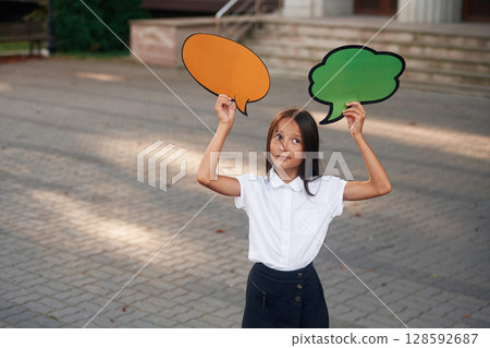 The choice. Holding banners with no text, copy space. School girl in uniform is outdoors near the building The choice. Holding banners with no text, copy space. School girl in uniform is outdoors near the building 128592687