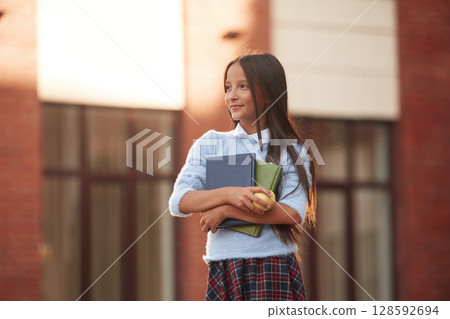 Conception of knowledge. School girl in uniform is outdoors near the building 128592694