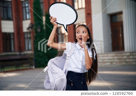 Sticker with thoughts, copy space for text. School girl in uniform is outdoors near the building Sticker with thoughts, copy space for text. School girl in uniform is outdoors near the building 128592760