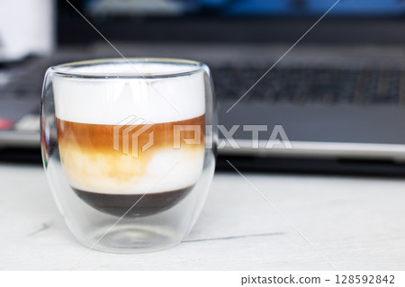 A close up of a cup of coffee in front of a laptop A close up of a cup of coffee in front of a laptop 128592842