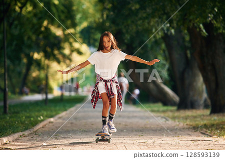 Controlling the balance. Happy little girl with skateboard outdoors Controlling the balance. Happy little girl with skateboard outdoors 128593139