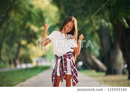 Celebrating success, happy. Young girl in casual clothes is in the public park outdoors Celebrating success, happy. Young girl in casual clothes is in the public park outdoors 128593160
