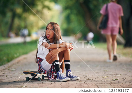 Showing the tongue. Happy little girl with skateboard outdoors 128593177