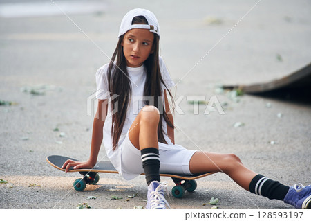 Sitting on the skateboard. Happy little girl is outdoors Sitting on the skateboard. Happy little girl is outdoors 128593197