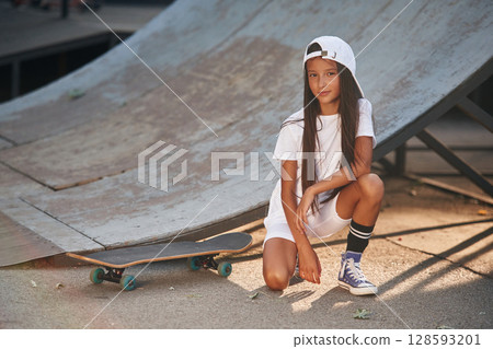 Ramp is behind. Girl is sitting. With skateboard outdoors Ramp is behind. Girl is sitting. With skateboard outdoors 128593201